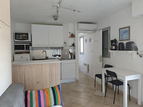 une cuisine avec des armoires blanches et une table et des chaises dans l'établissement Studio face mer avec clim, WiFi, parking privé, terrasse ensoleillée - FR-1-803-50, au Lavandou