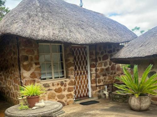 a stone house with a thatched roof and some plants at Augustine Avenue Guest House in Ladysmith
