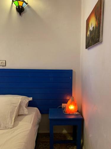 a bed with a blue headboard and a table with a lamp at Chez Youssef in Merzouga