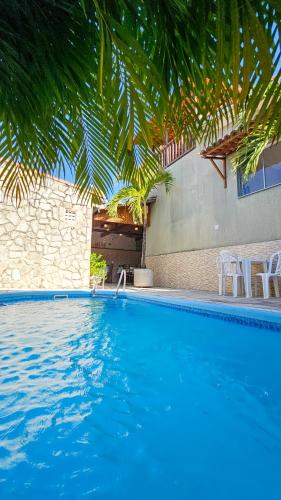 a blue swimming pool with chairs and a building at Morro Branco Pousada e aptos in Natal