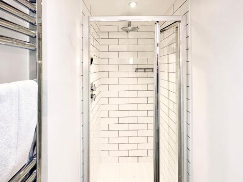 a glass shower door in a bathroom with white tiles at Spike by The Suffolk Cottage Collection in Chillesford