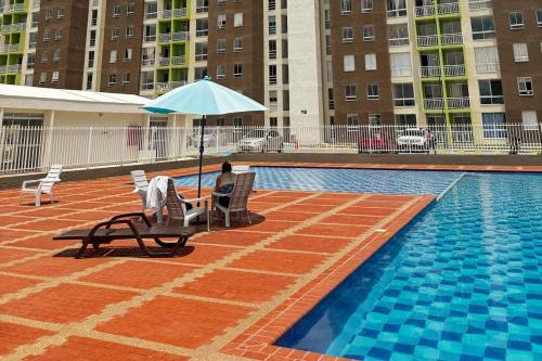 a person sitting in a chair under an umbrella next to a pool at Moderno apartamento con balcon y vista al guadual, Piscina y parqueadero in Pereira
