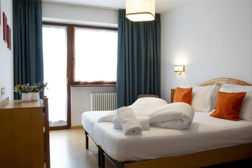 a bedroom with a bed with white sheets and orange pillows at Hotel Bonapace ***S in Madonna di Campiglio