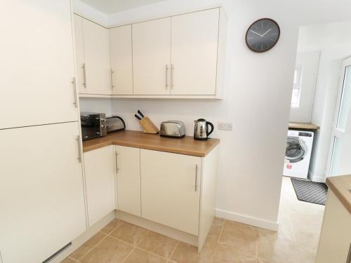 a kitchen with white cabinets and a clock on the wall at Twrog, 3 bedroom house in Blaenau-Ffestiniog