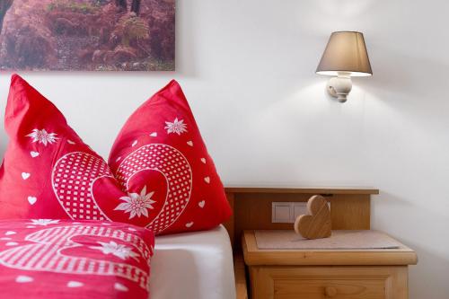 a bed with red pillows and a table with a lamp at Untertalhof in Castelrotto
