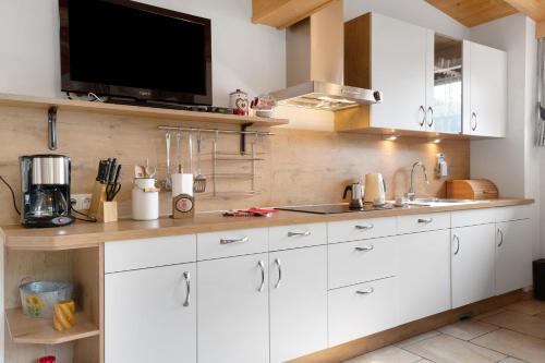 a kitchen with white cabinets and a flat screen tv at Untertalhof in Castelrotto