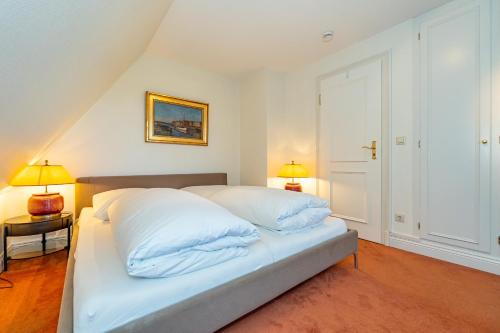a bedroom with a bed with white sheets and two lamps at Haus Daanshoog in Keitum