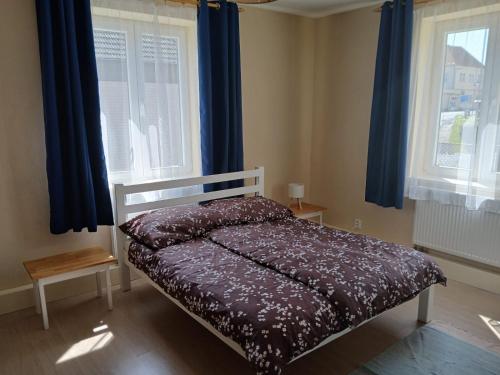 a bed in a room with two windows with blue curtains at Apartman Barrington in Žinkovy