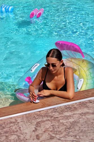 a woman sitting in a raft in a pool with a drink at Coast To Coast - Rooms & Pool! Camere moderne e piscina in Sant'Egidio del Monte Albino