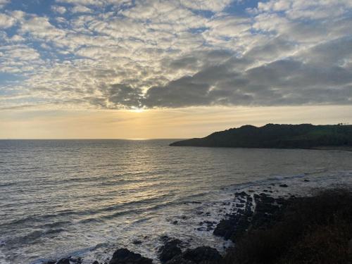 a sunset over the ocean with a rocky beach at Ground Floor - view of Lighthouse, Garden and Parking in Swansea