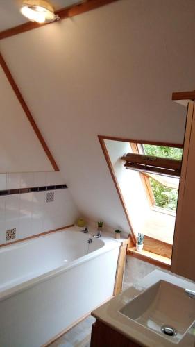 La salle de bains mansardée est pourvue d'une baignoire et d'un lavabo. dans l'établissement au petit bonheur, à Putanges