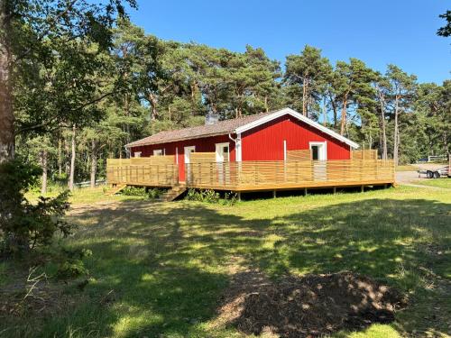 une grange rouge avec une terrasse en bois dans un champ dans l'établissement Kolonin Kuggaviken, à Åsa