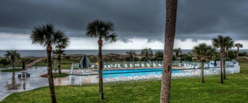 a pool with palm trees and chairs and the ocean at Days Inn & Suites by Wyndham Jekyll Island in Jekyll Island