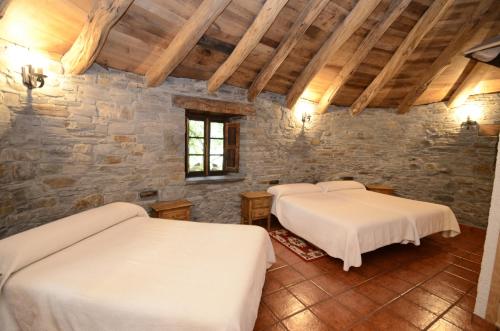 two beds in a room with a stone wall at El Rincón del Cuco in Tejedo de Ancares