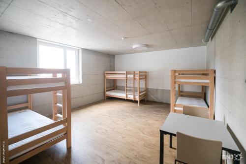 a room with bunk beds and a table and a window at Auberge de Jeunesse Saignelégier in Saignelégier