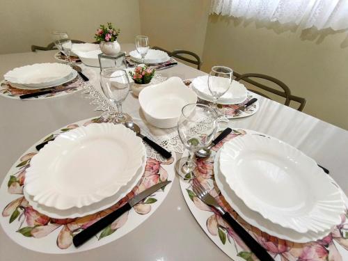 a table with white plates and wine glasses on it at CASA OT ESTRELA - Climatização, churrasqueira e piscina in Três Lagoas