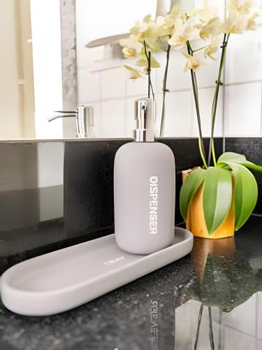 a white soap bottle sitting on a counter with flowers at Flat Belverede in Belo Horizonte