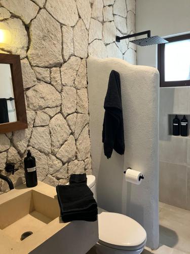 a bathroom with a white toilet and a stone wall at Casa Xunan - Beautiful 1 Bedroom Apartment with pool in Mahahual