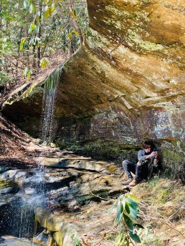 a man sitting on a rock next to a waterfall at The Goldfinch's Nest - Glamping Tent with AC in Rogers