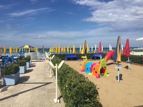 un parque infantil con sombrillas y equipo de juegos en la playa en Hotel Marina, en Fano