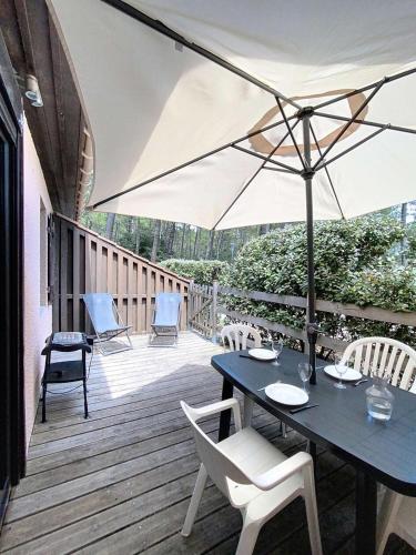 une terrasse en bois avec une table et un parasol dans l'établissement Residence Les Pins - Petite maison mitoyenne 2 chambres, 4 personnes à Lacanau océan, résidence les pins MAE-0381, à Lacanau