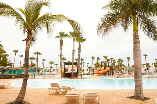 a pool at a resort with palm trees and a slide at Oasis Dunas Corralejo in Corralejo