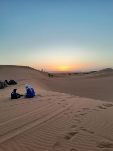 two people sitting in the desert watching the sunset at Safari luxury camp in Merzouga