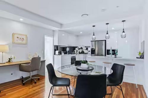 a white kitchen with a glass table and chairs at Park Ave Retreat - 3 Carparks, WiFi, BBQ, King Bed in Brisbane