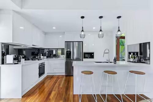 a white kitchen with wooden floors and white counter tops at Park Ave Retreat - 3 Carparks, WiFi, BBQ, King Bed in Brisbane