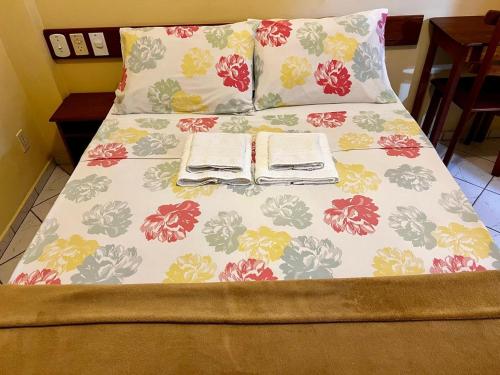 a bed with a floral bedspread and two pillows at Pousada Maravista in Anchieta