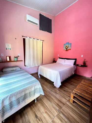 two beds in a room with pink walls and wooden floors at Pousada - Casa dos Paiva in Barreirinhas