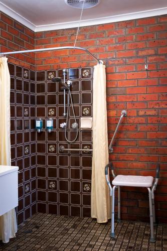 a bathroom with a brick wall with a shower and a chair at Golden Country Motel and Caravan Park in Maryborough