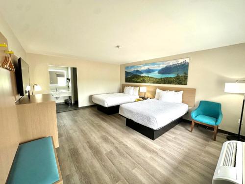 a hotel room with two beds and a blue chair at Days Inn & Suites by Wyndham Bossier City - Casino Area in Bossier City