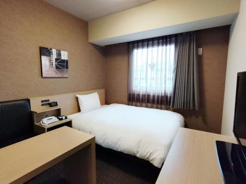 a hotel room with a bed and a window at Hotel Route-Inn Takaoka Ekimae in Takaoka