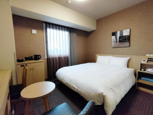 a hotel room with a large bed and a table at Hotel Route-Inn Takaoka Ekimae in Takaoka