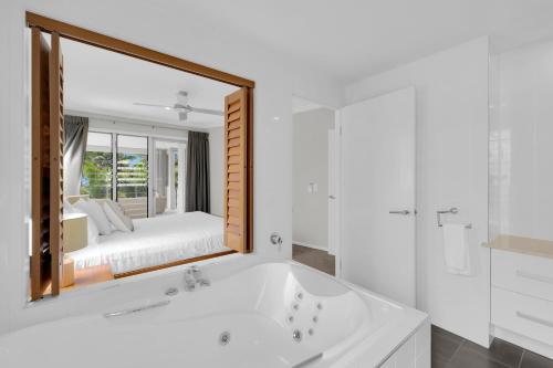 un bagno bianco con vasca e specchio di Turquesa Tides - Beachfront Resort Living a Palm Cove