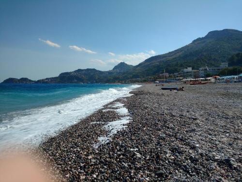 a rocky beach with the ocean and mountains in the background at Polifemo in Letojanni