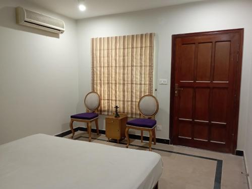 a bedroom with two chairs and a bed and a door at Morgah Resort - Guest Rooms in Rawalpindi