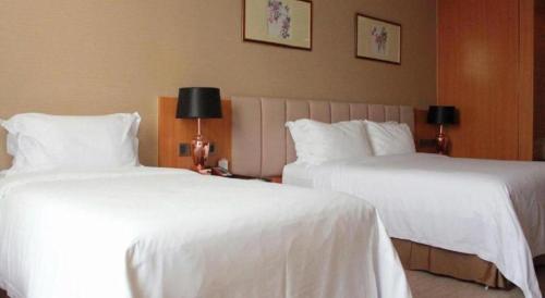 two beds in a hotel room with white sheets at Zhangjiagang Zhonglian GDH International Hotel in Zhangjiagang