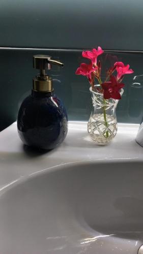Una botella de perfume y un jarrón de flores en un lavabo. en Tiny home at the castle, en Shkodër