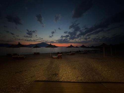 a sunset on a beach with umbrellas and the ocean at Nettuno Resort Orikum in Orikum