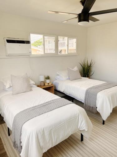 two beds in a room with white walls and windows at Hale Moana Retreat AC Walk to Ocean and Spacious Family Stay in Laie