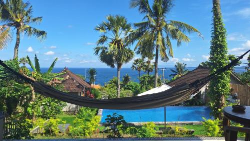 a hammock in front of a resort with a pool at Frangipani Inn & Restaurant in Seraya