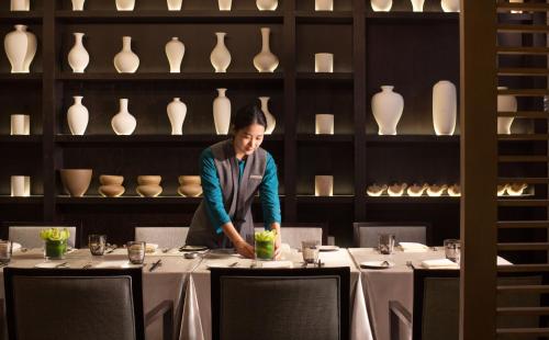 a woman standing at a table in a restaurant with vases at Cheery Dragon Canal Hotel Hangzhou - Intangible Cultural Heritage Hotel in Hangzhou