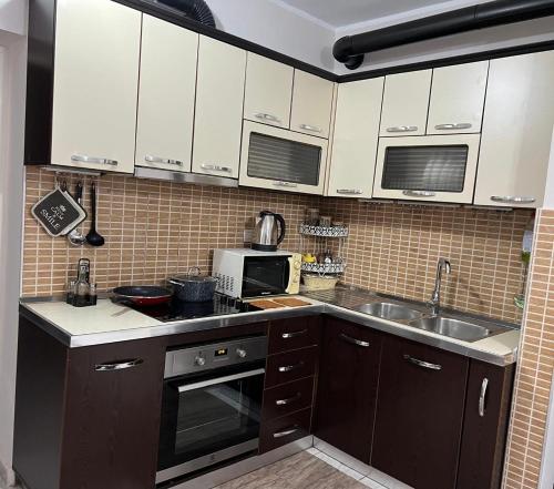 Una cocina con gabinetes blancos, un fregadero y un microondas. en Home Shkodra Center, en Shkodër