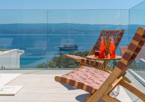 a table and two chairs on a balcony with a boat in the water at Luxurious VILLA LAPIS - heated pool, sauna, gym and spa, 120m to sandy beach in Omiš