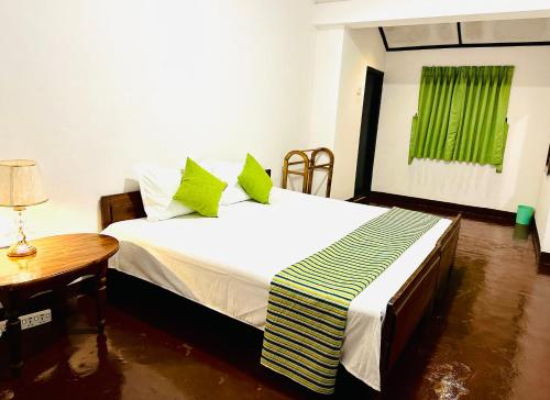 a bedroom with a bed with green pillows and a table at Rose hotel in Bandarawela