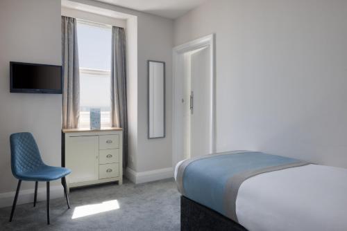 a bedroom with a bed and a chair and a television at The Cumberland Hotel in Eastbourne