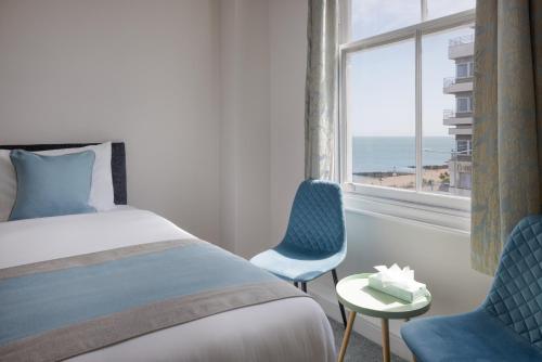 a bedroom with a bed and two chairs and a window at The Cumberland Hotel in Eastbourne