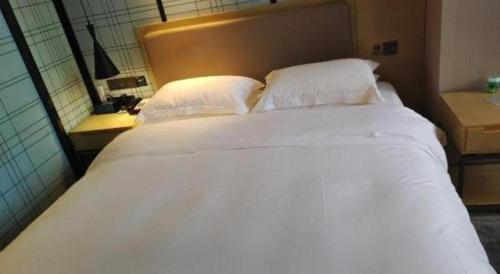 a bed with white sheets and pillows in a room at Echarm Hotel Xiangyang Erqi in Xiangyang